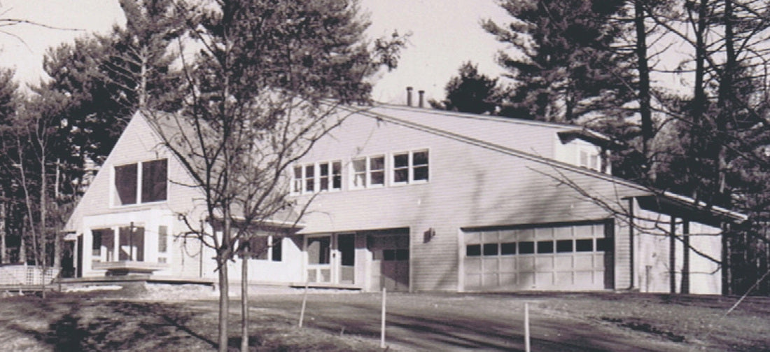 A black and white photograph of a modern single-story house with a large garage, surrounded by tall trees.