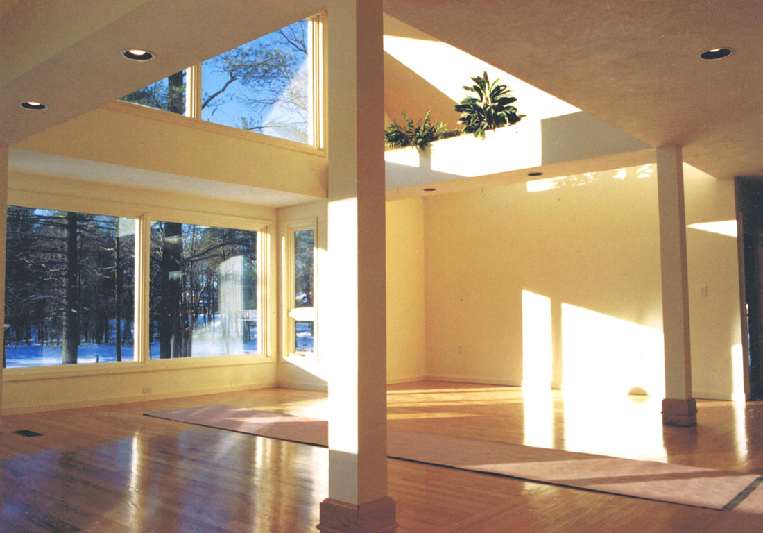 An empty, modern multi-level room with high ceilings, large windows showing a snowy outdoor view, polished wood floors, and warm yellow walls.
