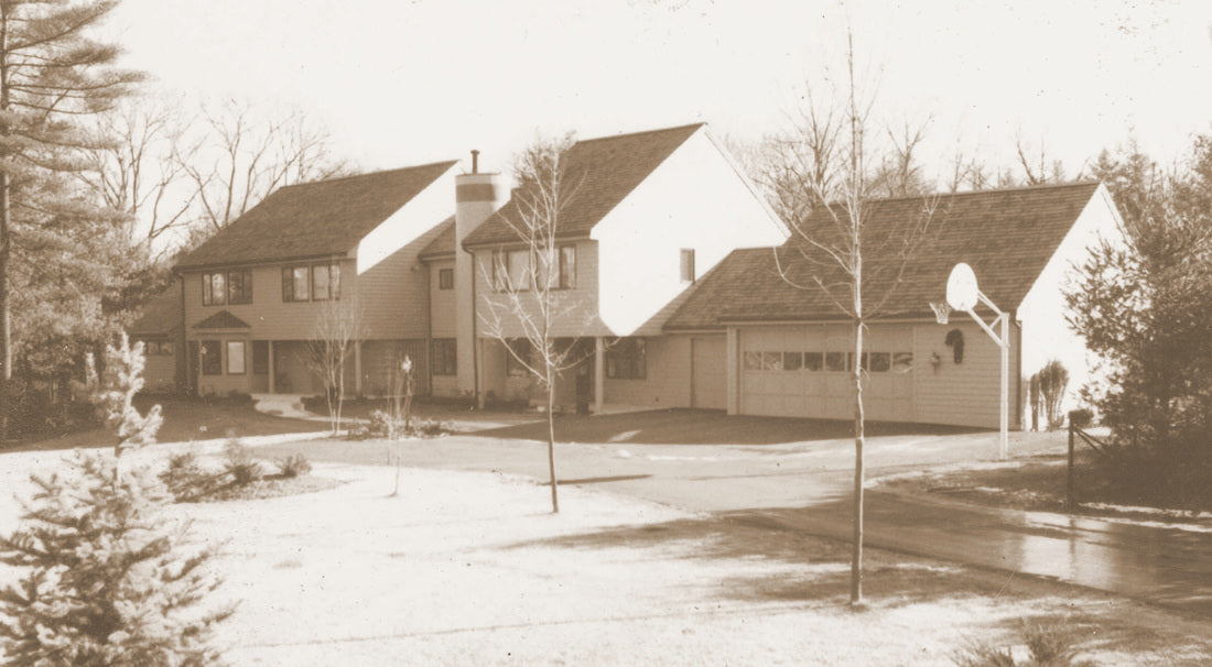 A sepia-toned photograph of a large suburban house with a detached garage, front yard, trees, and a basketball hoop near the garage.