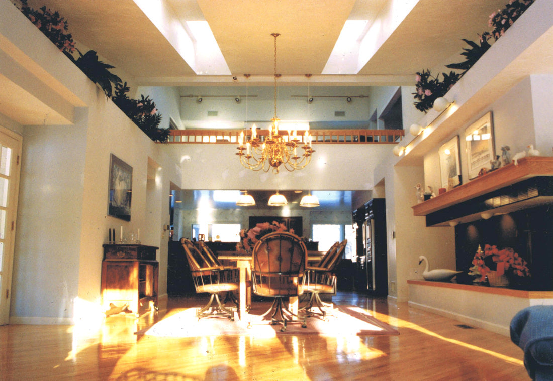 A high-ceilinged dining room with hardwood floors, a chandelier, a dining table and chairs, built-in shelving, and a fireplace on the right side.