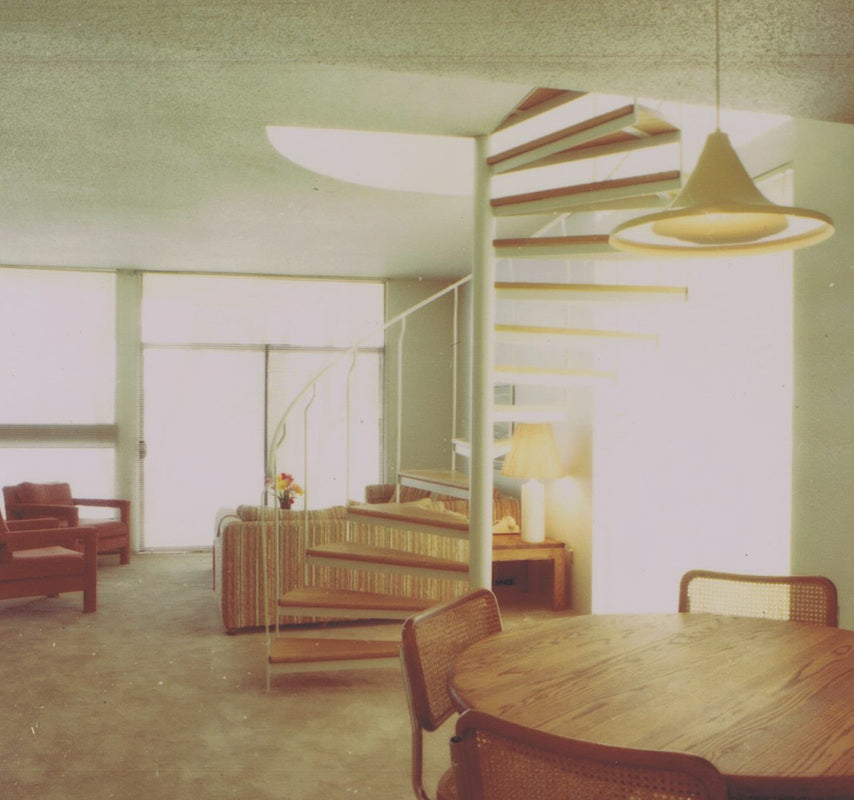 Interior of a condominium at the Inn of the Sea Resort in Ladysmith, British Columbia, featuring an open dining and living area, spiral staircase to a loft, vaulted ceiling, and floor-to-ceiling windows overlooking the resort grounds.