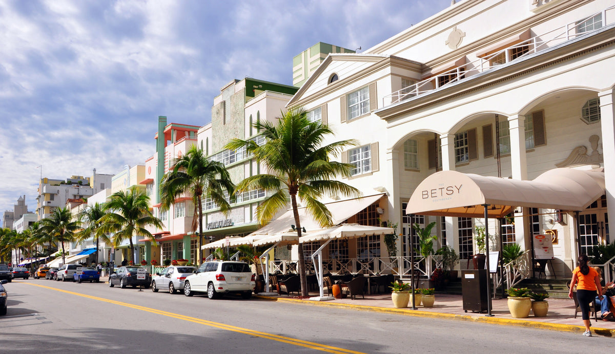 Street scene of South Beach in Florida with palm trees, cars, and a building with an awning in a city setting.
