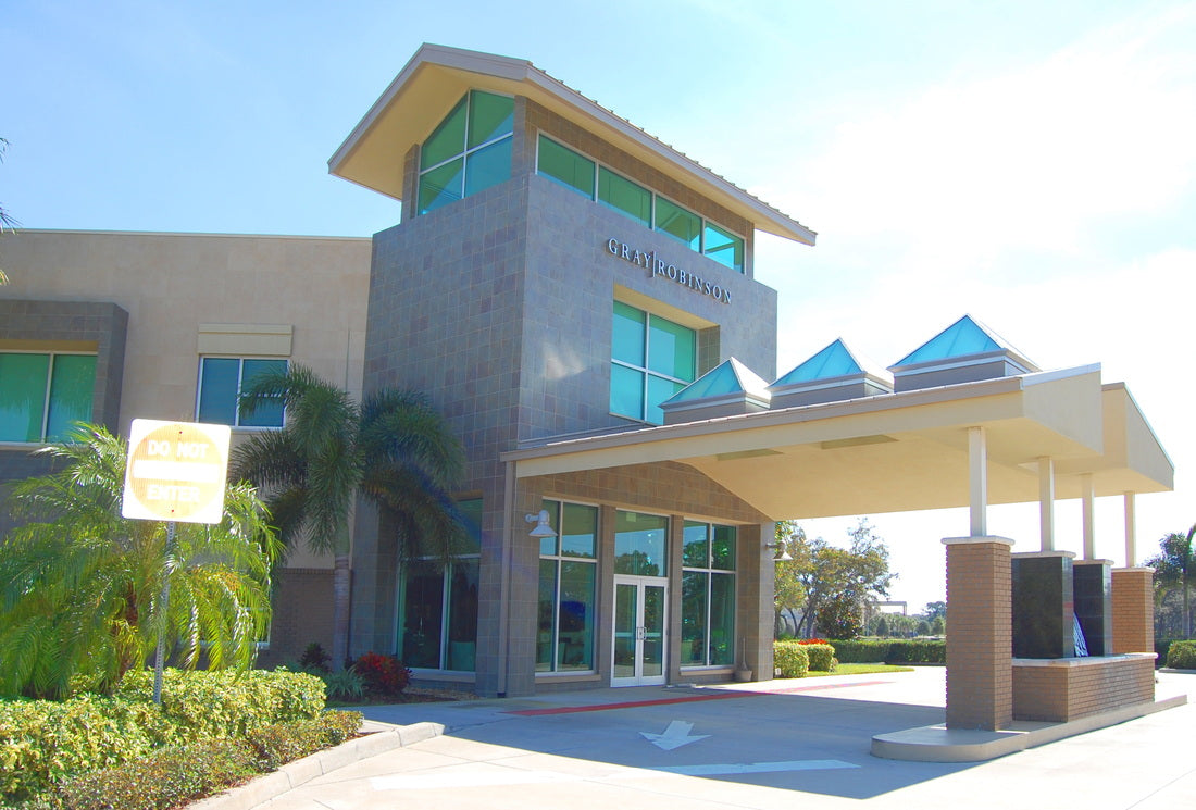 Angled view of the completed GrayRobinson office building in Melbourne, Florida, highlighting the three-story glass and stone entry tower, covered porte-cochère, and contemporary commercial architecture with tropical landscaping.