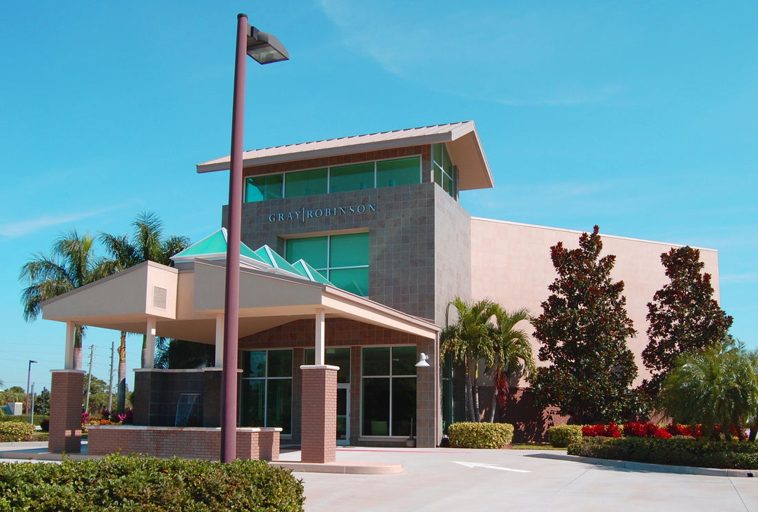 Front view of the completed GrayRobinson office building in Melbourne, Florida, featuring a contemporary three-story entrance tower, covered porte-cochère with integrated fountain, and tropical landscaping.